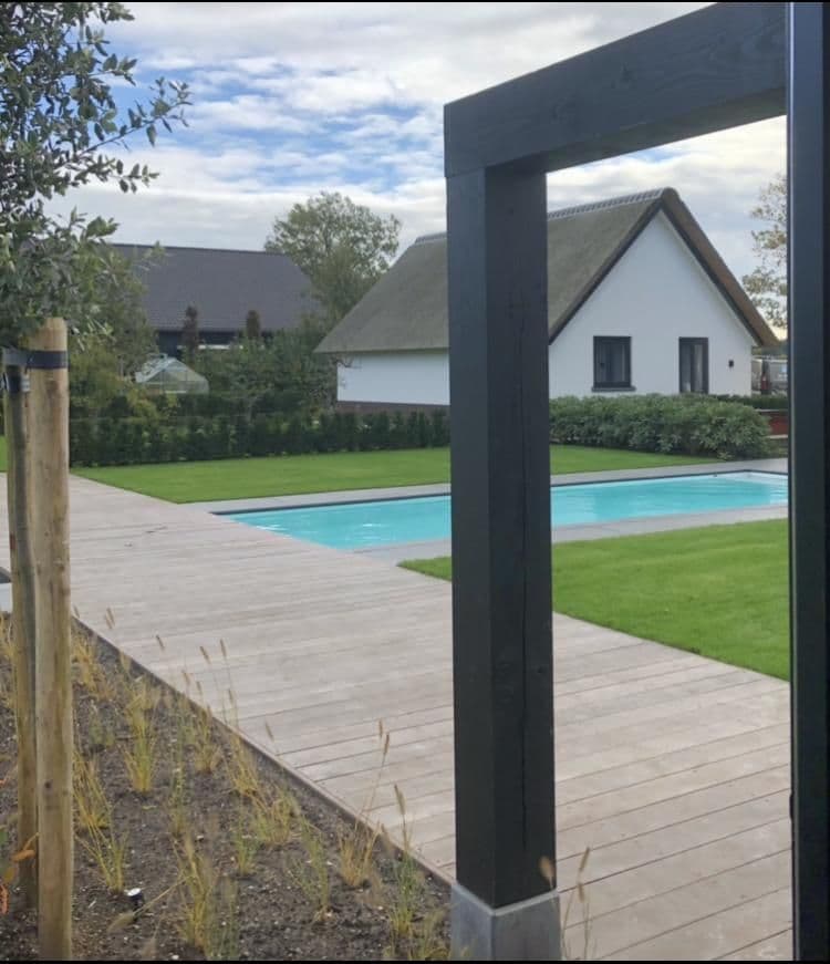 Achtertuin met zwembad, houten vlonder, grasveld en wit huis met hellend dak