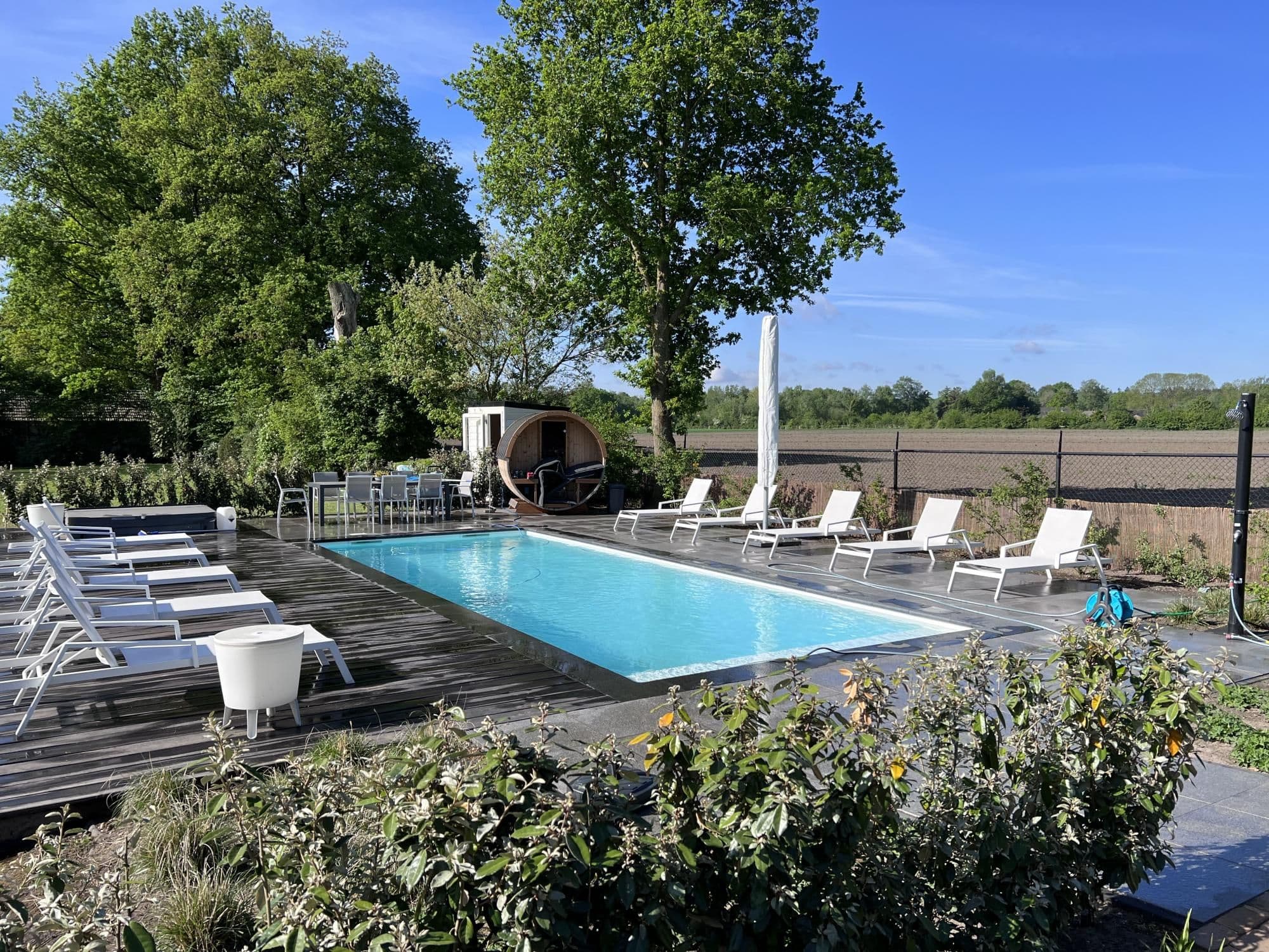 Buitenzwembad met helder water, witte ligstoelen op houten terras en bomen op de achtergrond