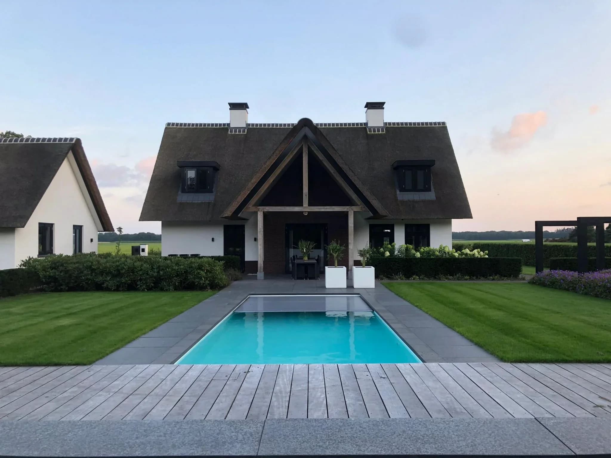 Voorgevel van een huis met rieten dak, twee dakkapellen, houten entree en een rechthoekig zwembad op de voorgrond