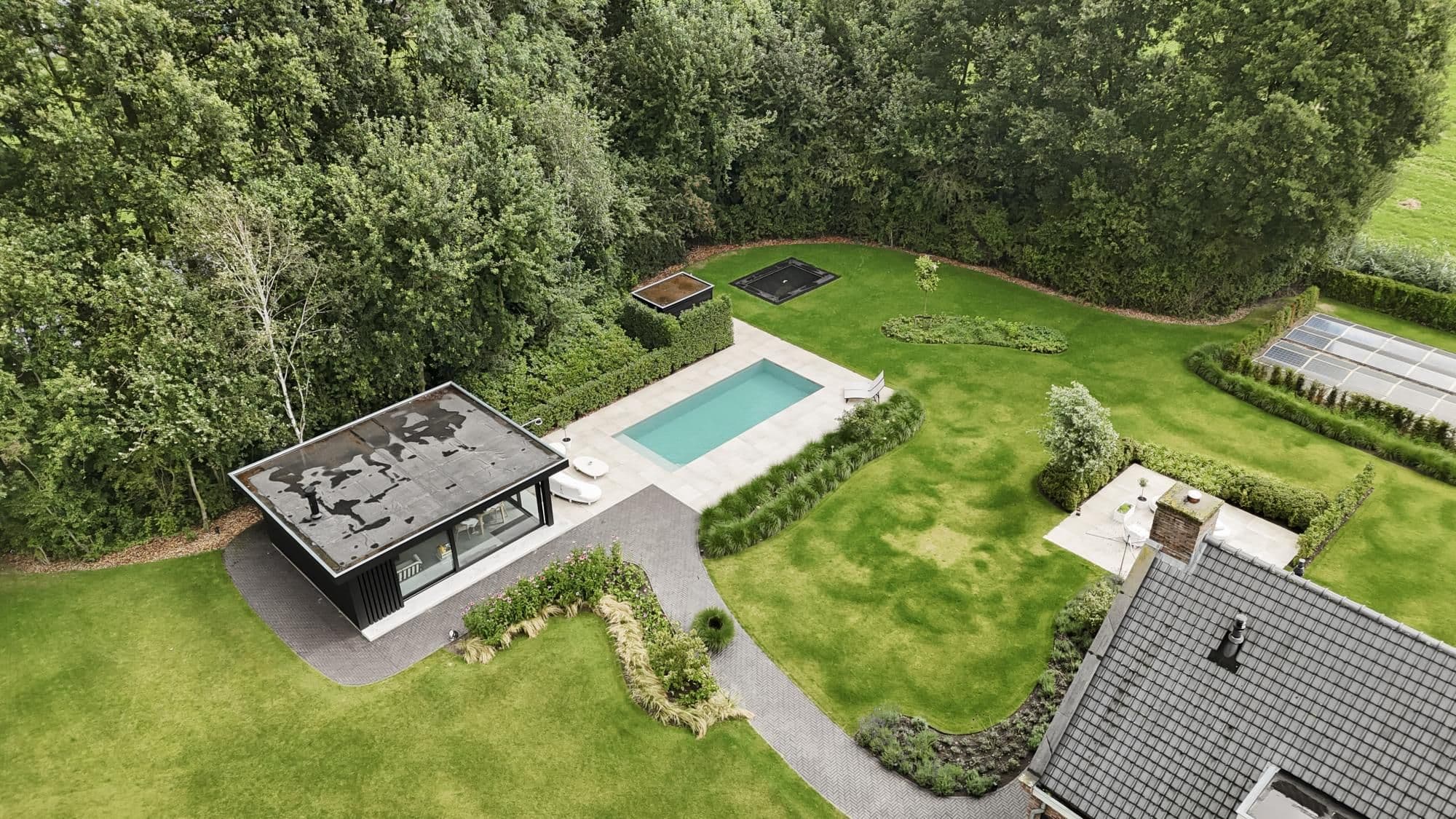 Luchtfoto van een achtertuin met modern bijgebouw met plat dak, rechthoekig buitenzwembad, paden en omringende bomen