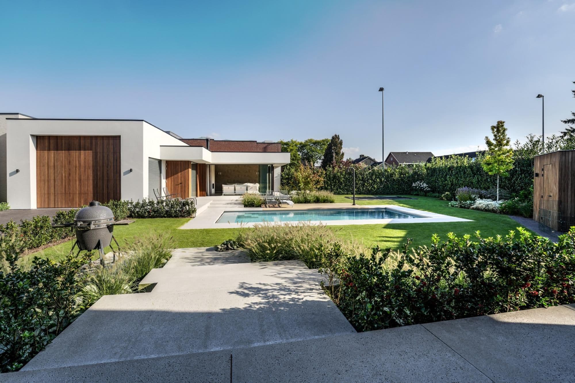 Modern huis met houten garagedeur, terras met lounge, zwembad, grasveld en aangelegde borders