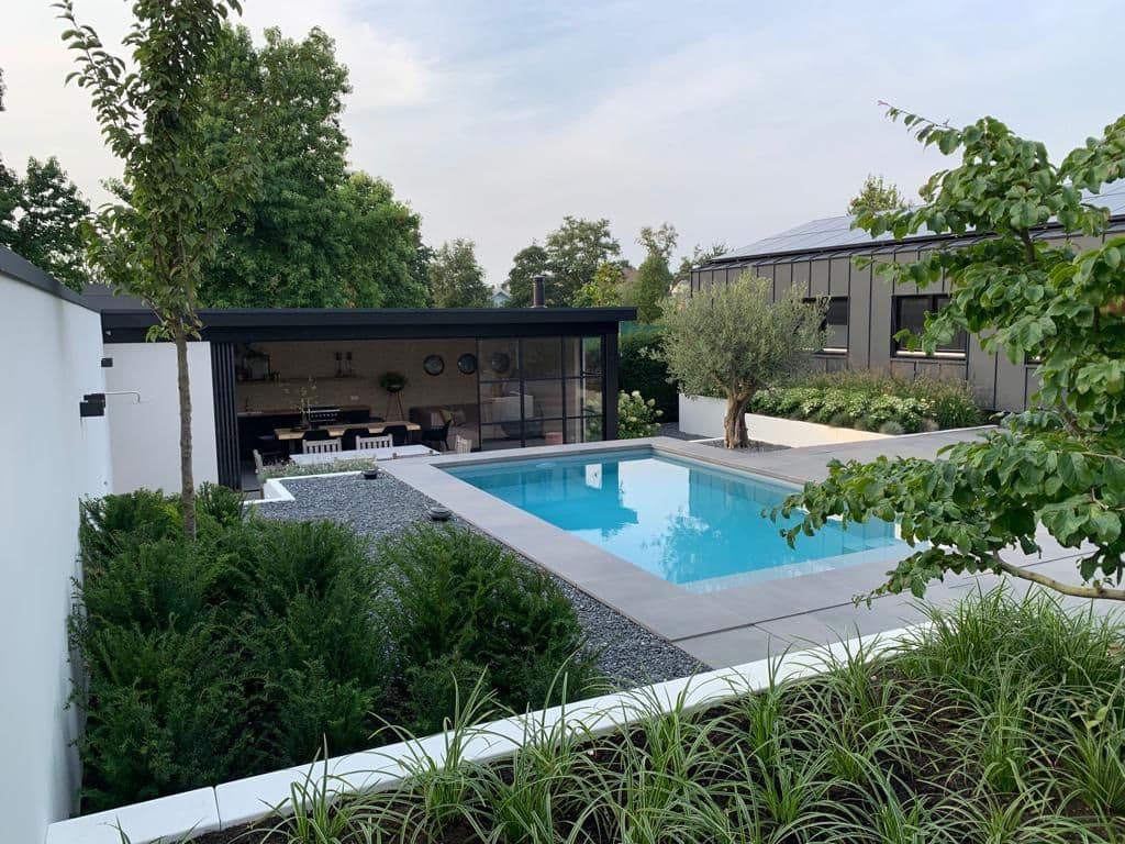 Rechthoekig zwembad in een moderne tuin met bestrating, planten en een overdekte zithoek met eettafel