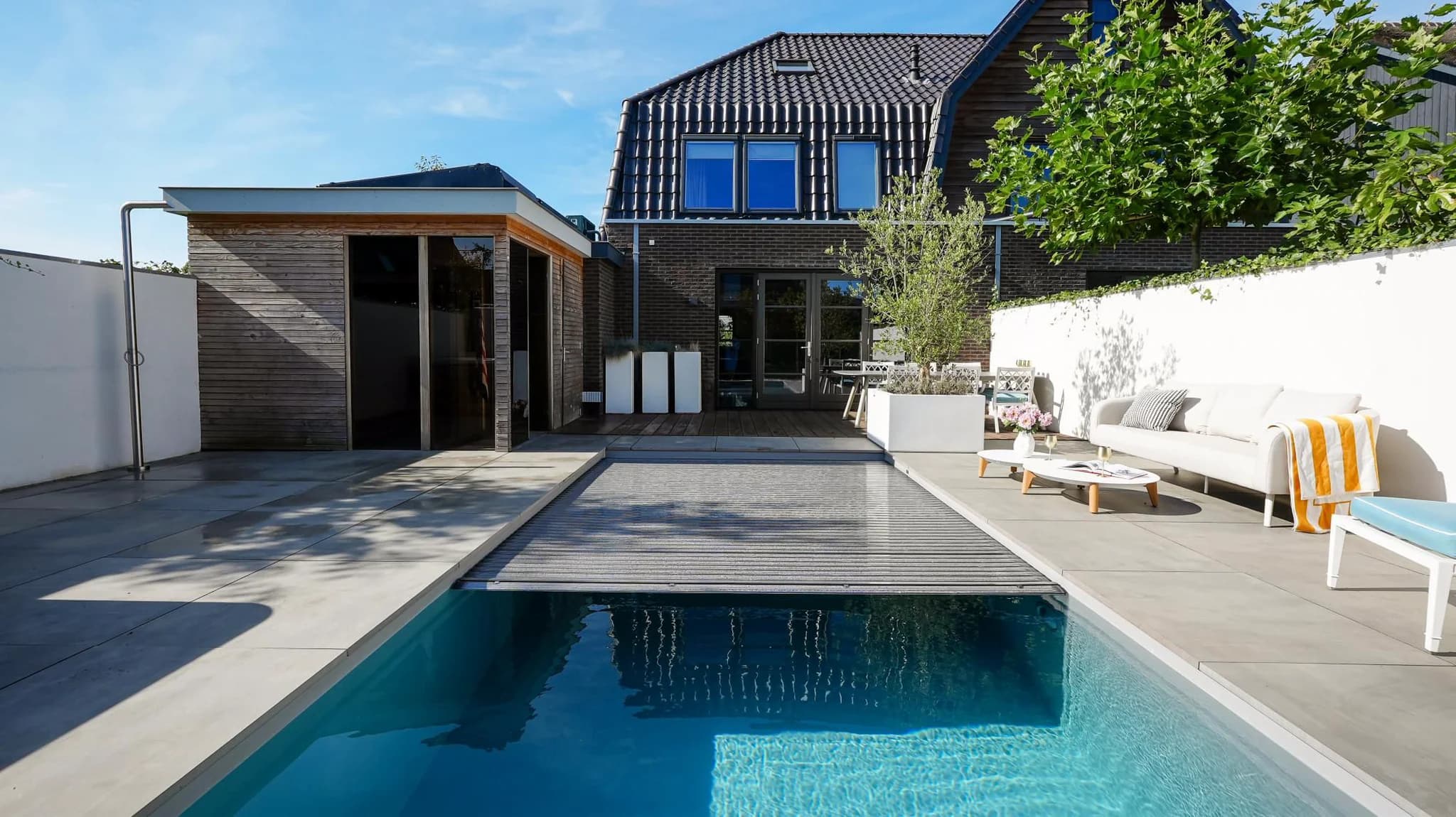 Modern huis met houten uitbouw, betegeld terras, buitenbank en zwembad met deels gesloten afdekking