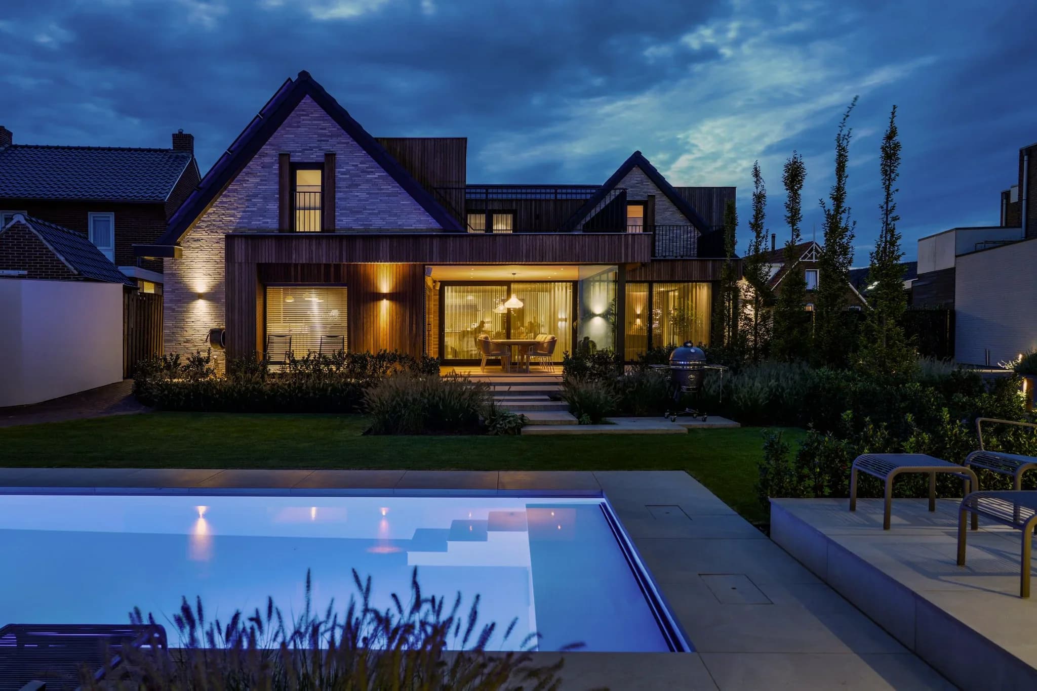 Moderne woning met verlichte woonkamer, tuin en zwembad in de avondschemering