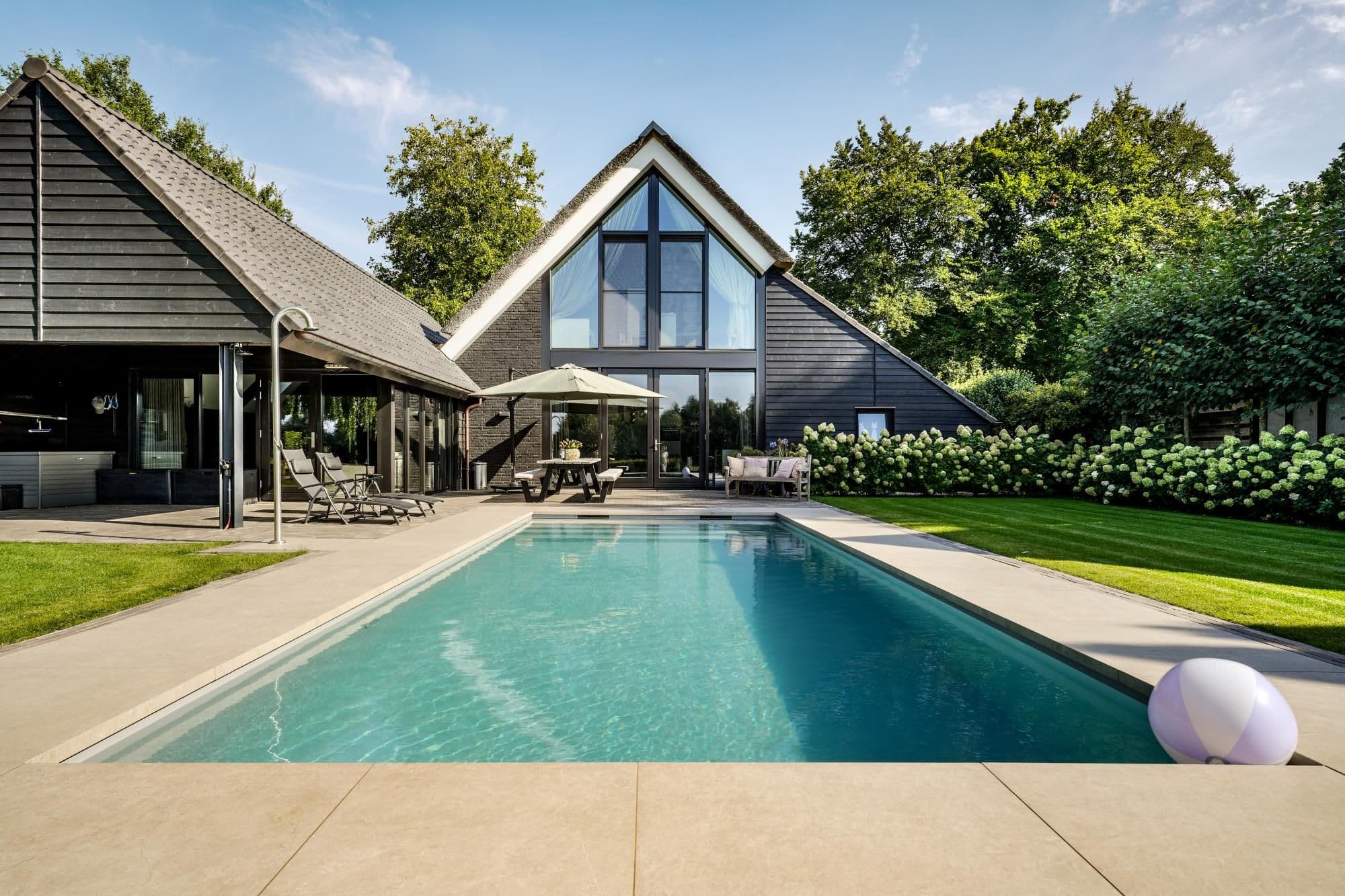 Moderne woning met grote glasgevel, terras met parasol en ligstoelen en een rechthoekig zwembad op de voorgrond