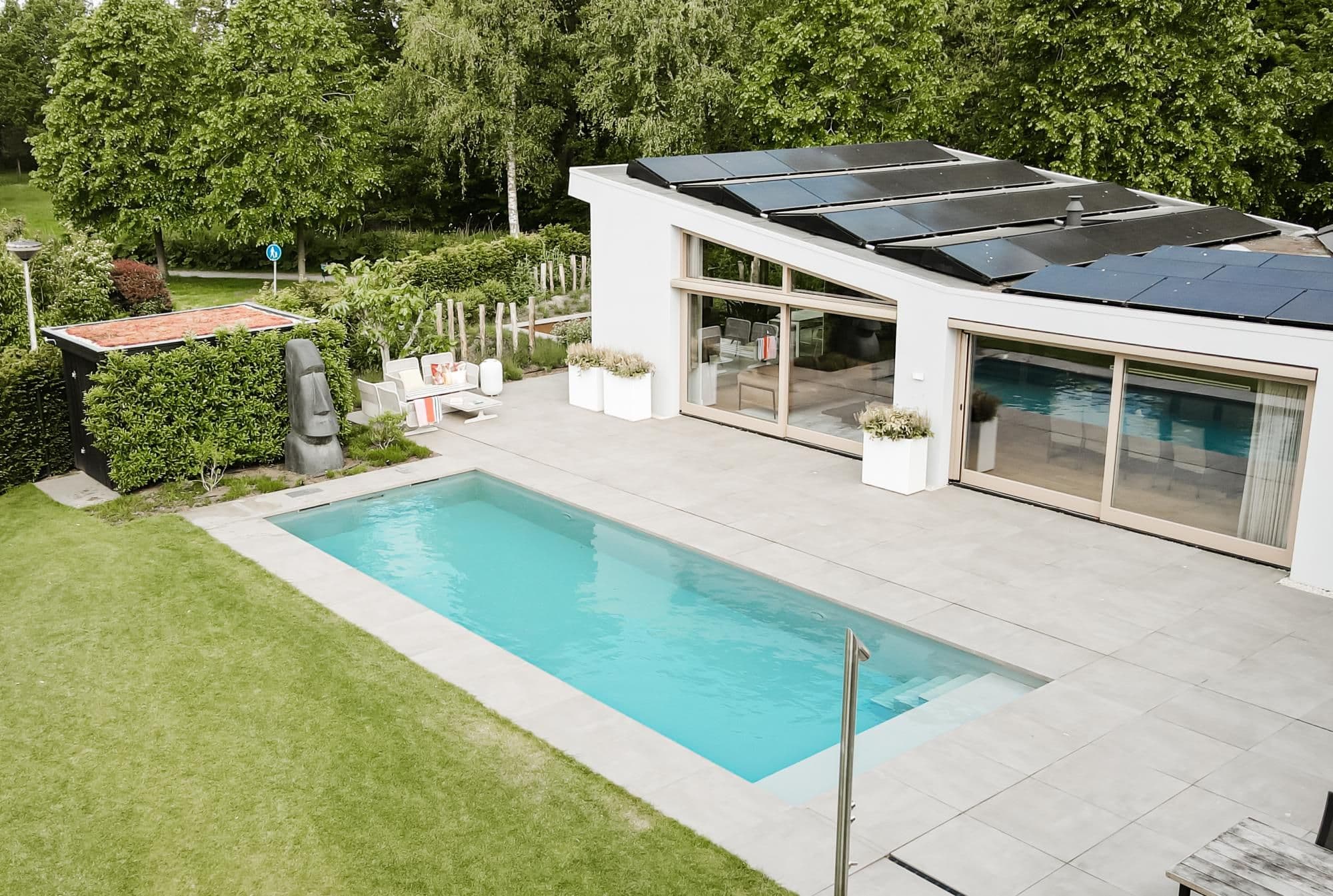 Moderne woning met schuin dak en zonnepanelen, rechthoekig buitenzwembad, betegeld terras met zitmeubilair en groene tuin