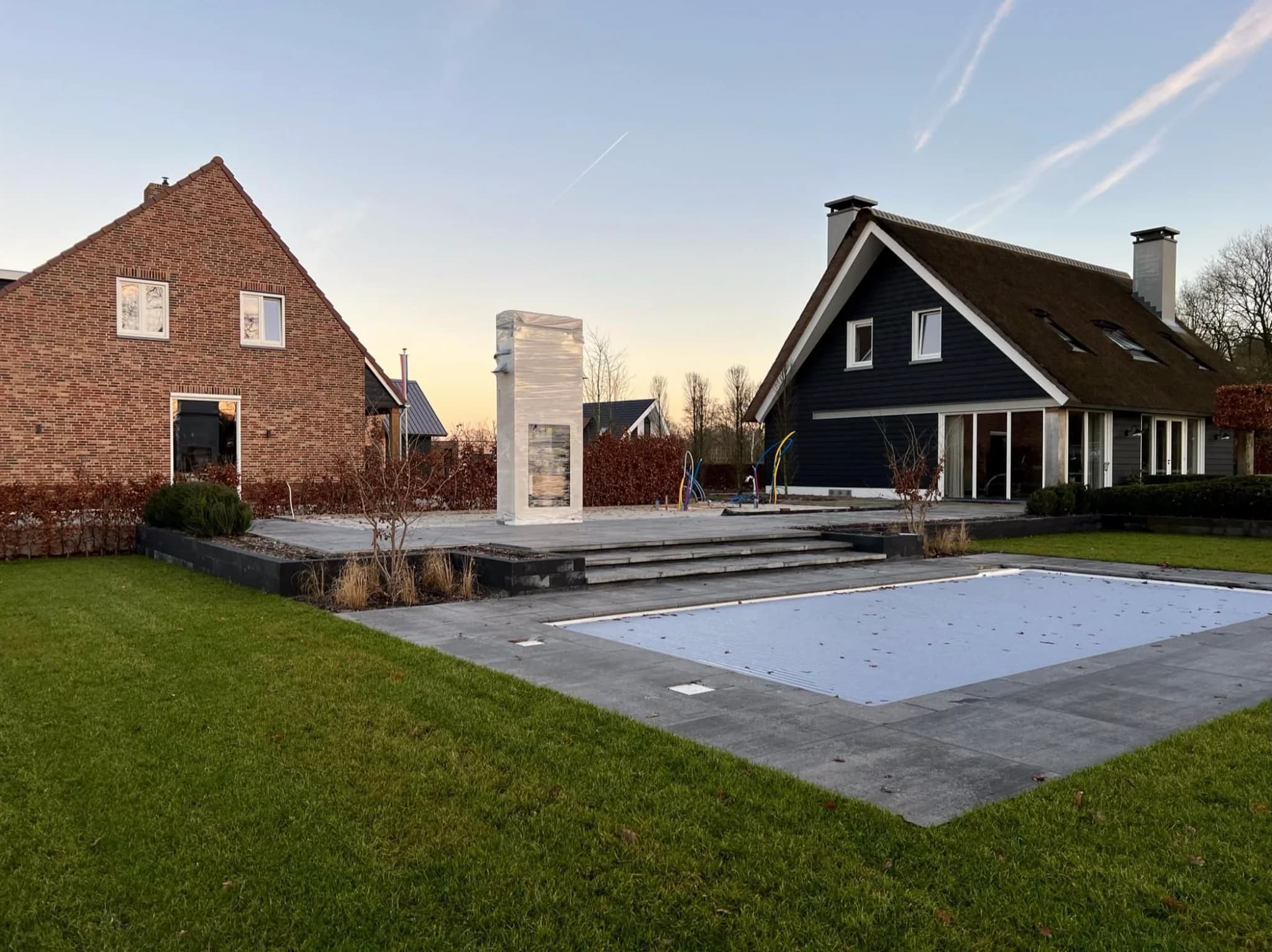Twee huizen met patio, afgedekt zwembad en ingepakt object bij avondlicht