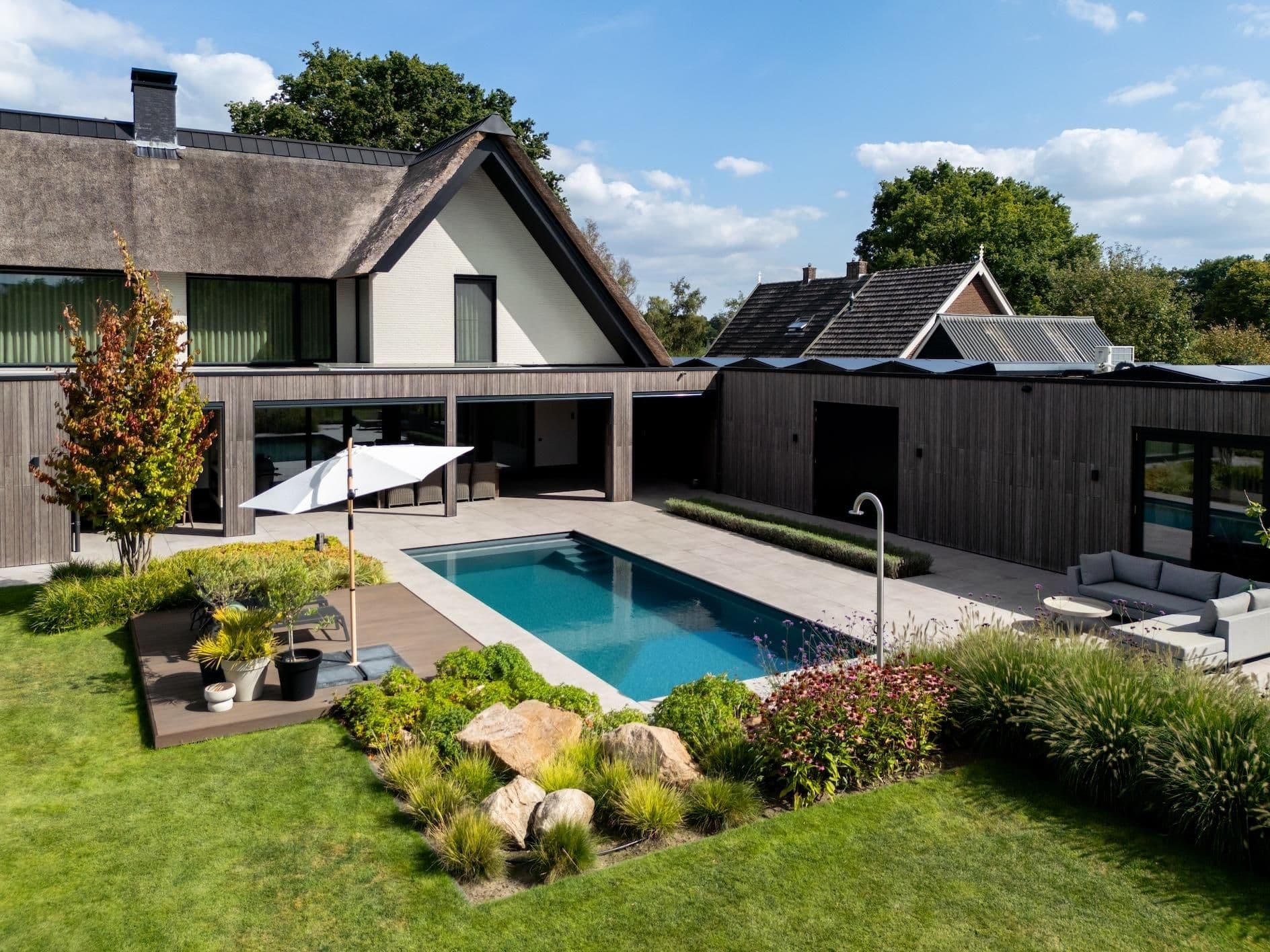 Modern woonhuis met rieten dak, houten gevel, buitenzwembad, parasol op het terras en onderhouden tuin