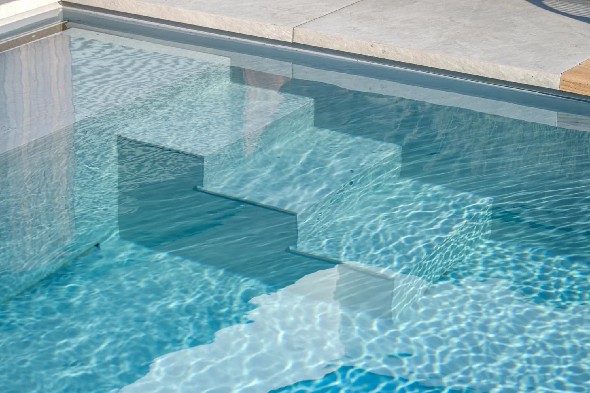 Close-up van zwembadtrap met lichtgekleurde treden en helder blauw water met golfpatroon en zonreflecties